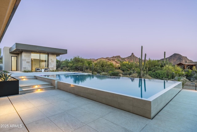 pool at dusk featuring a mountain view and a patio