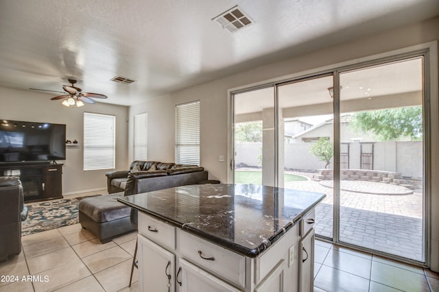 kitchen with dark stone counters, white cabinets, light tile patterned floors, a kitchen island, and ceiling fan