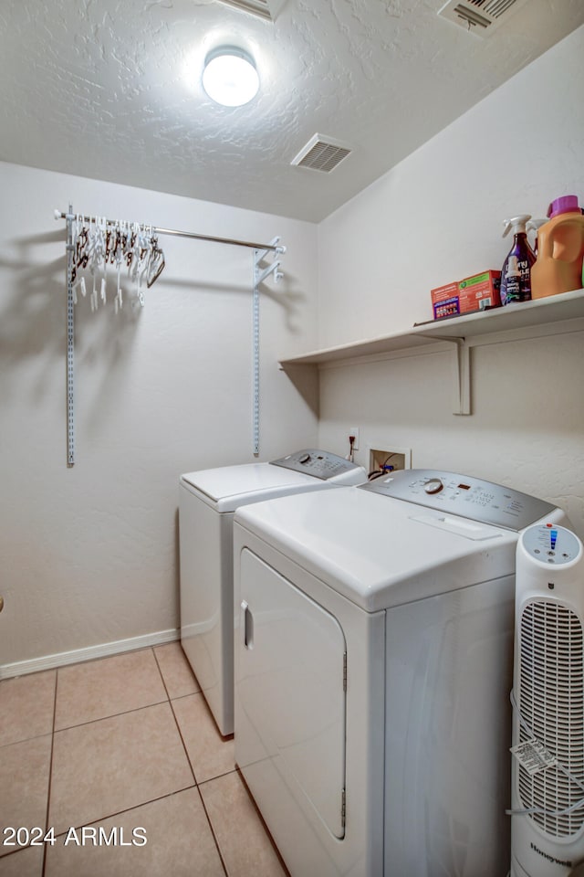 washroom with washing machine and dryer, a textured ceiling, and light tile patterned floors