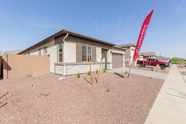 view of front of house featuring a garage, fence, driveway, stone siding, and stucco siding