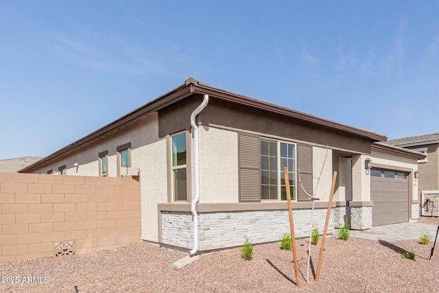 view of front of house featuring a garage, stone siding, fence, and stucco siding