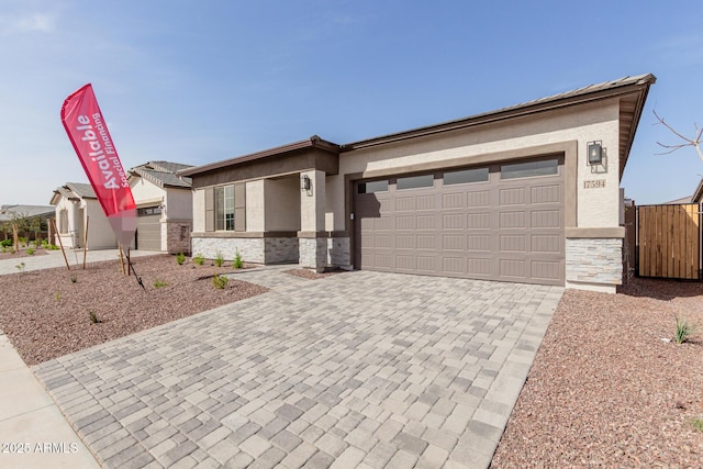 view of front of house with an attached garage, stone siding, decorative driveway, and stucco siding