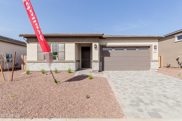 prairie-style home featuring a garage, stone siding, decorative driveway, and stucco siding