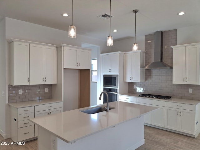 kitchen featuring a center island with sink, stainless steel appliances, visible vents, a sink, and wall chimney exhaust hood