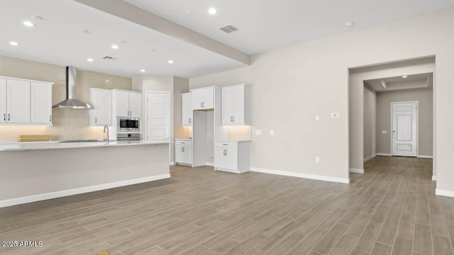 kitchen featuring sink, white cabinets, stainless steel appliances, light wood-type flooring, and wall chimney exhaust hood