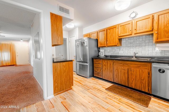 kitchen with sink, a textured ceiling, light hardwood / wood-style flooring, backsplash, and appliances with stainless steel finishes