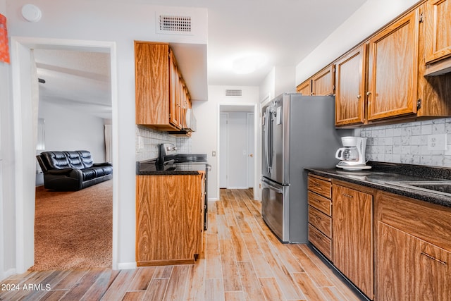 kitchen featuring decorative backsplash, dark stone countertops, stainless steel appliances, and light wood-type flooring