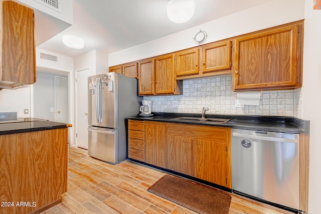 kitchen featuring appliances with stainless steel finishes, light wood-type flooring, sink, and backsplash