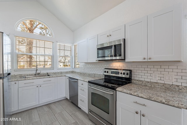 kitchen featuring vaulted ceiling, appliances with stainless steel finishes, sink, white cabinets, and backsplash