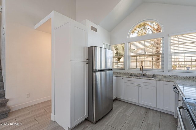 kitchen featuring sink, white cabinetry, range, stainless steel refrigerator, and light stone countertops