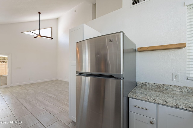 kitchen featuring stainless steel refrigerator, ceiling fan, hanging light fixtures, high vaulted ceiling, and light stone counters