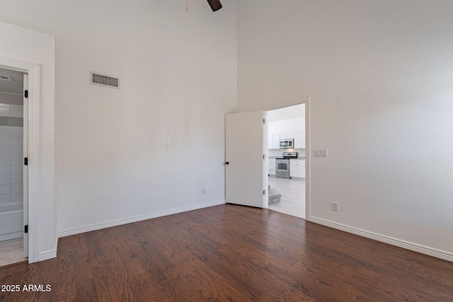 empty room featuring ceiling fan, a towering ceiling, and dark hardwood / wood-style flooring