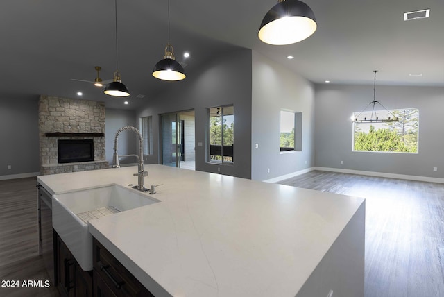 kitchen featuring hardwood / wood-style floors, a kitchen island with sink, pendant lighting, a stone fireplace, and sink