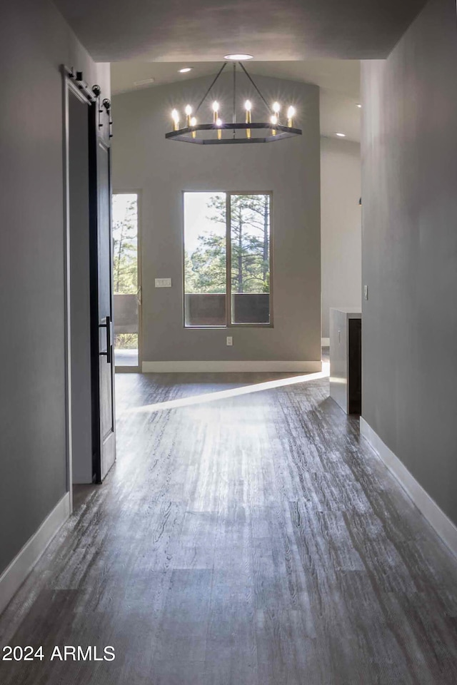 unfurnished dining area featuring vaulted ceiling, an inviting chandelier, dark hardwood / wood-style flooring, and a barn door