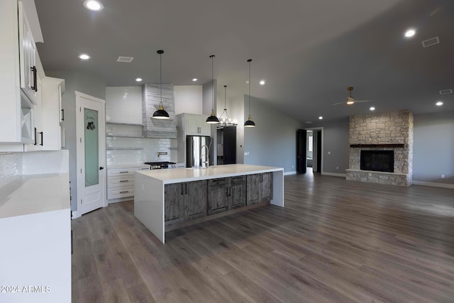 kitchen featuring a large island with sink, white cabinetry, dark hardwood / wood-style floors, a stone fireplace, and decorative light fixtures