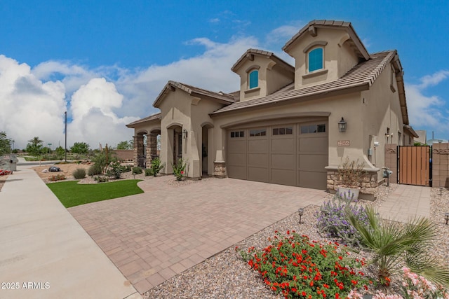 mediterranean / spanish-style home with stucco siding, a gate, decorative driveway, an attached garage, and stone siding