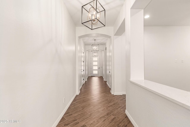 hall with arched walkways, a chandelier, dark wood finished floors, baseboards, and recessed lighting