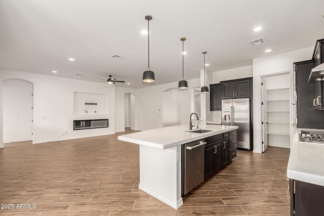 kitchen with appliances with stainless steel finishes, arched walkways, a sink, light countertops, and wood finished floors
