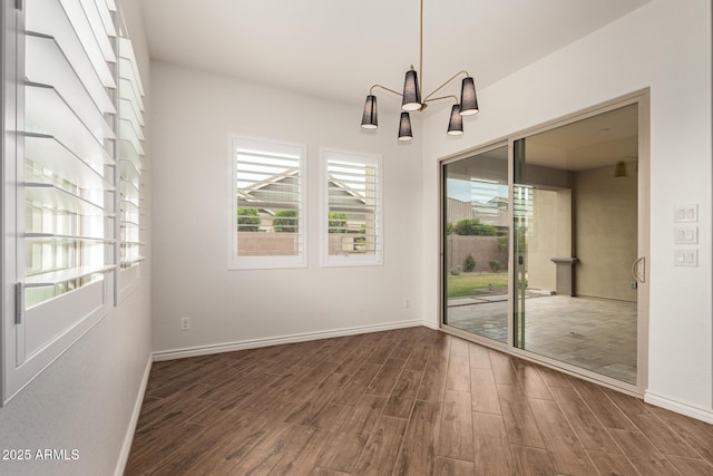 unfurnished dining area featuring wood finished floors, a chandelier, and baseboards