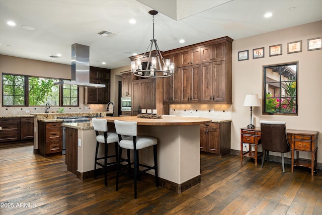 8454 E Leaning Rock Rd, Scottsdale, AZ 85266 - kitchen with dark wood-style flooring, an inviting chandelier, island exhaust hood, an island with sink, and visible vents
