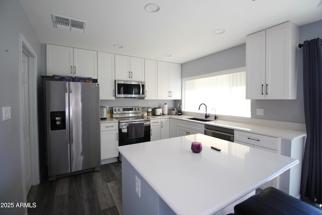 kitchen with sink, appliances with stainless steel finishes, a center island, white cabinets, and dark hardwood / wood-style flooring