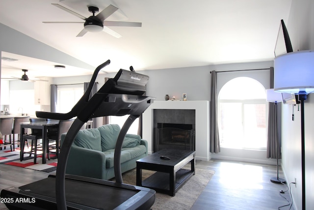 exercise room with ceiling fan, a tile fireplace, vaulted ceiling, and hardwood / wood-style floors