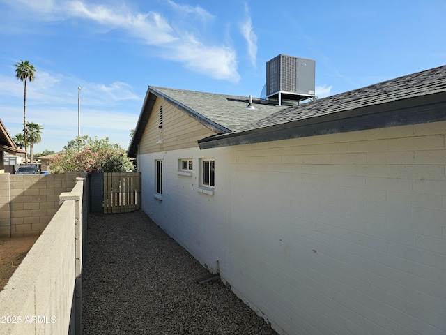 view of side of property with cooling unit, roof with shingles, and fence