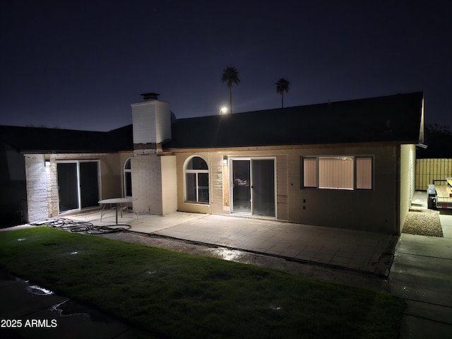 back of house at twilight featuring a chimney and a patio