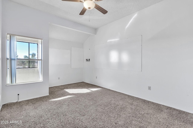 empty room with lofted ceiling with beams, ceiling fan, carpet floors, and a textured ceiling