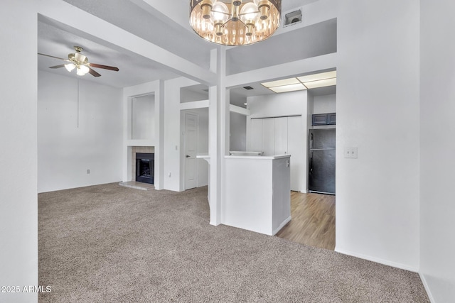 unfurnished living room with ceiling fan with notable chandelier, light colored carpet, and a tile fireplace