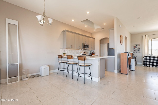 kitchen featuring arched walkways, light countertops, stainless steel microwave, decorative backsplash, and a peninsula