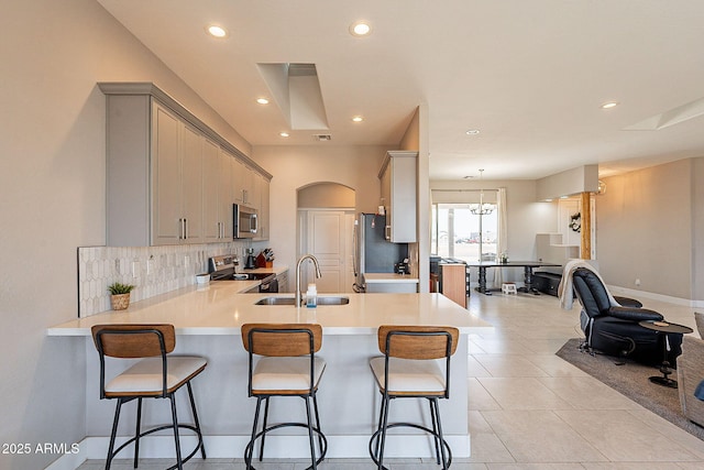 kitchen featuring open floor plan, a peninsula, stainless steel appliances, light countertops, and a sink