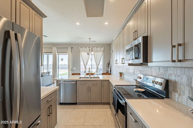 kitchen with appliances with stainless steel finishes, a peninsula, light countertops, pendant lighting, and a sink