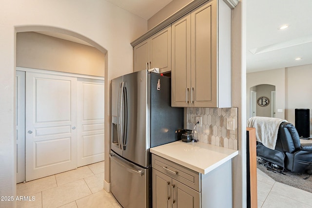 kitchen featuring arched walkways, light tile patterned floors, light countertops, decorative backsplash, and stainless steel fridge