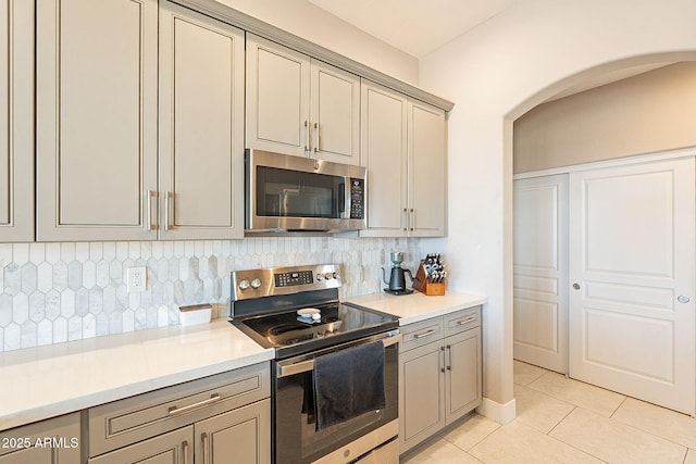 kitchen featuring arched walkways, light tile patterned floors, light countertops, decorative backsplash, and appliances with stainless steel finishes