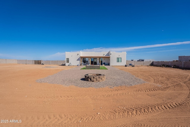 rear view of property with an outdoor fire pit, fence, and stucco siding