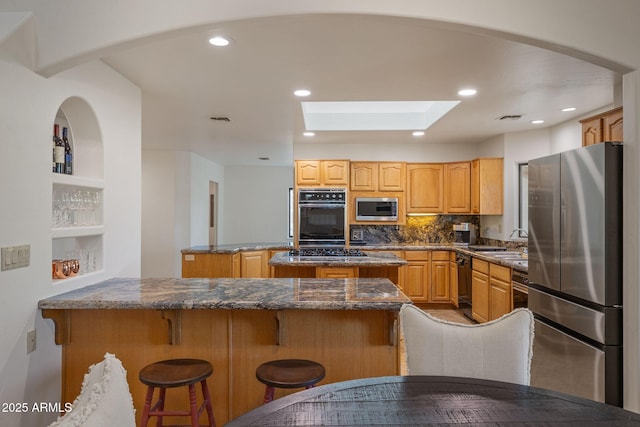 kitchen featuring a center island, visible vents, black appliances, a peninsula, and a kitchen bar