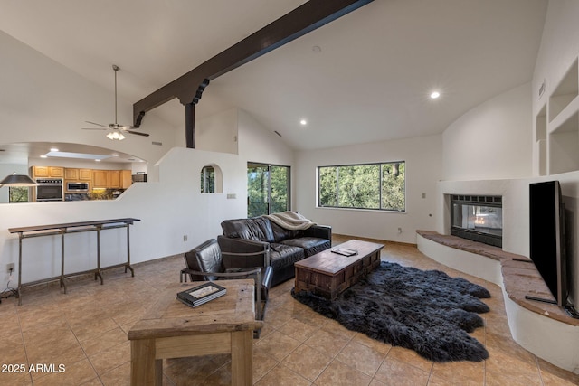 living area with beam ceiling, light tile patterned floors, a glass covered fireplace, ceiling fan, and high vaulted ceiling