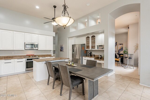 9678 E Voltaire Dr, Scottsdale, AZ 85260 - kitchen with appliances with stainless steel finishes, arched walkways, a ceiling fan, glass insert cabinets, and light tile patterned floors
