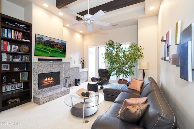 living room featuring ceiling fan, carpet flooring, beamed ceiling, and a tiled fireplace