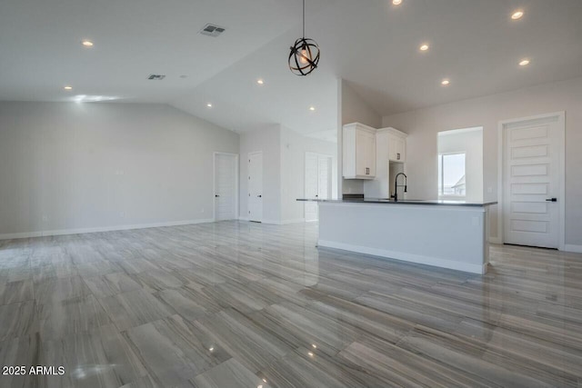 kitchen with high vaulted ceiling, sink, a center island with sink, and white cabinets