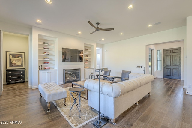 living room featuring dark wood-type flooring, built in features, and ceiling fan