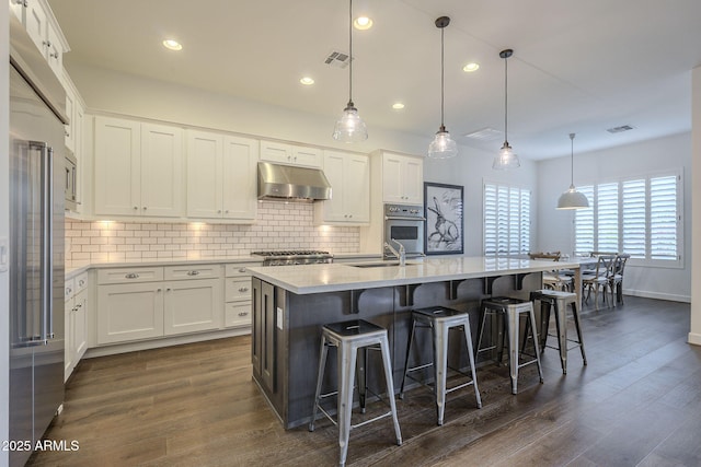 kitchen featuring white cabinetry, sink, decorative light fixtures, and a center island with sink