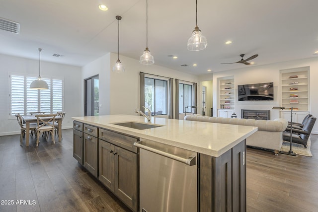 kitchen featuring pendant lighting, sink, dark hardwood / wood-style flooring, stainless steel dishwasher, and a center island with sink