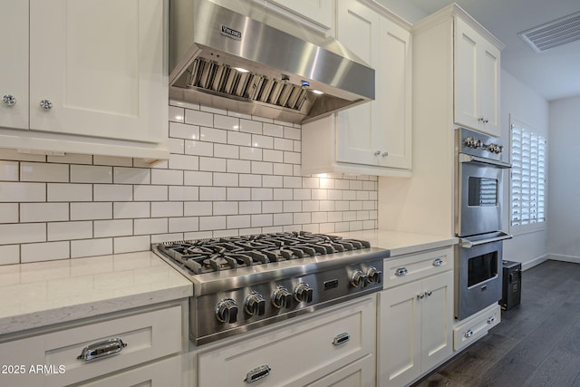 kitchen with white cabinetry, backsplash, stainless steel appliances, ventilation hood, and light stone countertops