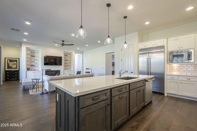 kitchen with pendant lighting, sink, white cabinets, built in appliances, and light stone counters