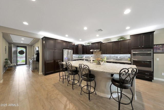 3359 E Penedes Dr, Gilbert, AZ 85298 - kitchen with stainless steel appliances, backsplash, a breakfast bar, light wood-type flooring, and baseboards
