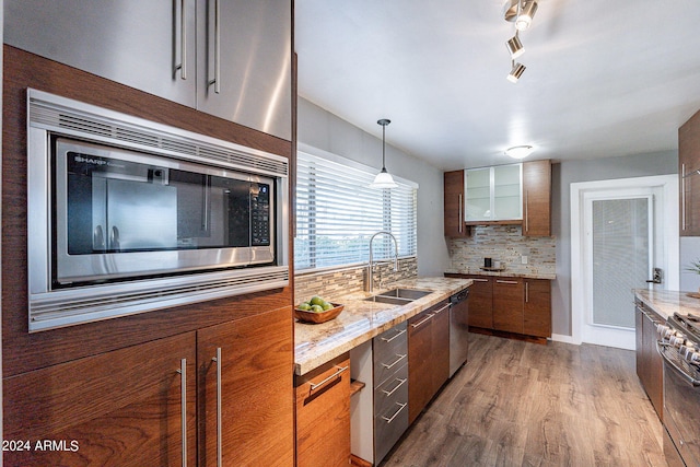 kitchen featuring wood finished floors, a sink, appliances with stainless steel finishes, decorative backsplash, and light stone countertops