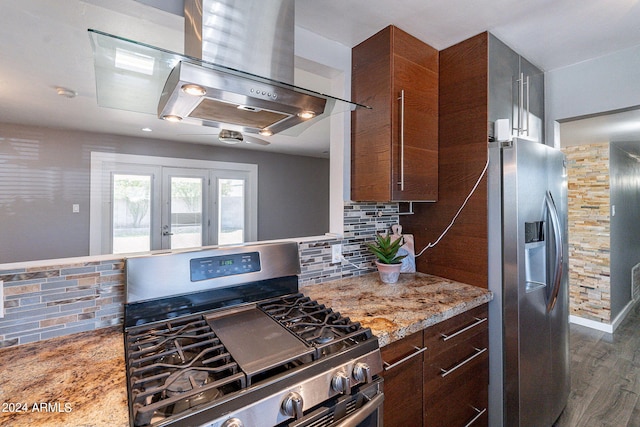 kitchen featuring light stone counters, dark wood-style flooring, stainless steel appliances, decorative backsplash, and exhaust hood