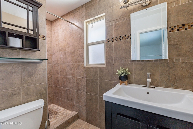 bathroom with a tile shower, tile walls, toilet, and vanity